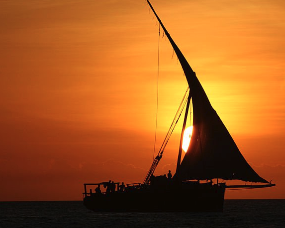 Traditional dhow sailboat silhouetted against sunset