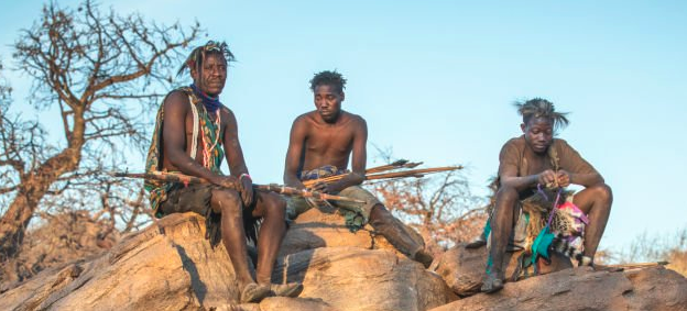 Three Hadzabe hunters sitting on rocks with traditional bows and arrows
