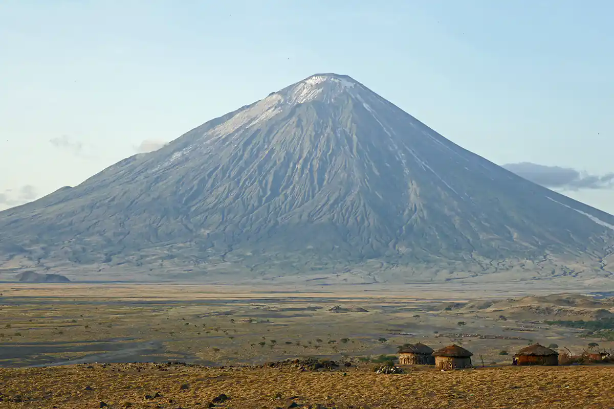 Oldonyo Lengai mountain rising from the Rift Valley with traditional Maasai huts in foreground